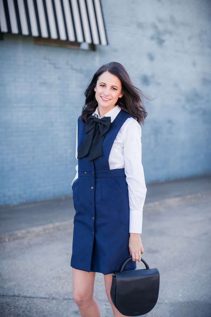 Amanda Miller wearing a black bow tie and white button up tunic under a navy pinafore dress
