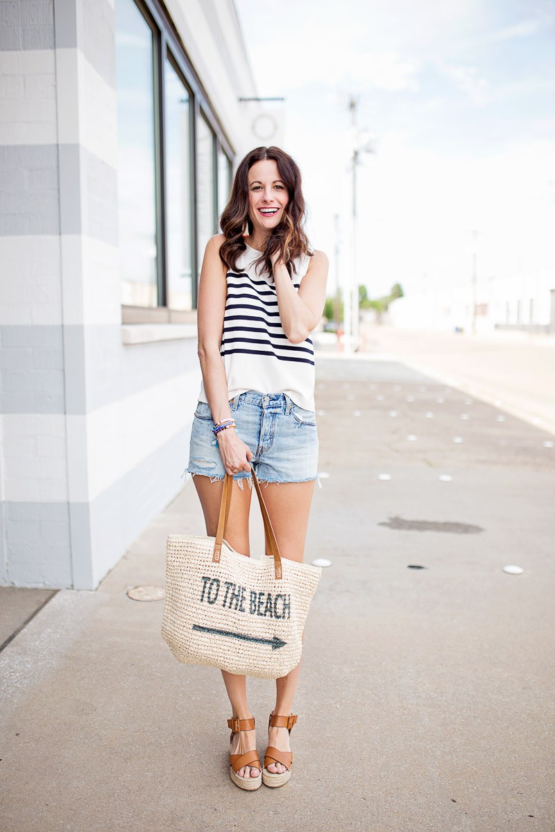 Amanda Miller holding a beach tote wearing distressed denim shorts and a navy striped top