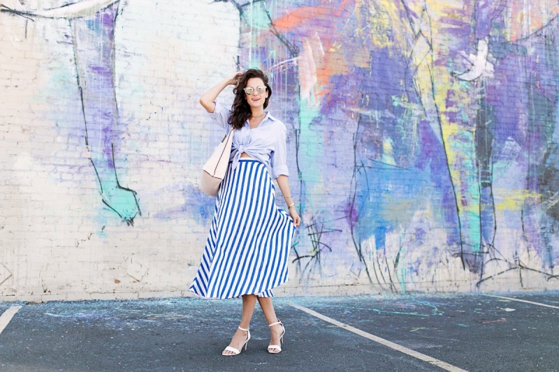 The Miller Affect wearing a blue and white midi skirt, a pink tote, and white heels