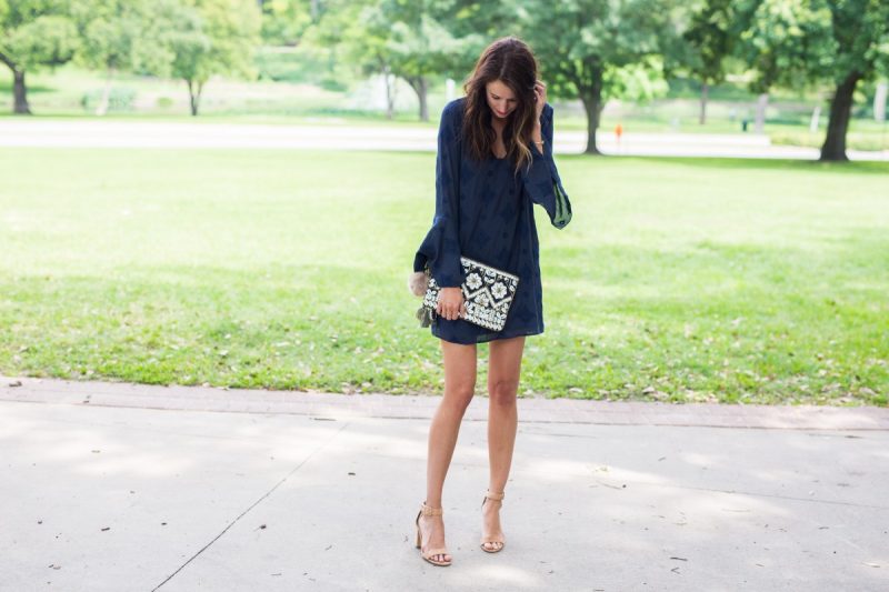 The Miller Affect wearing a navy bell sleeved dress and a shell clutch