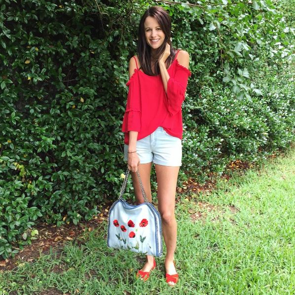 The Miller Affect wearing a red could shoulder ruffle top and carrying a Stella McCartney tote