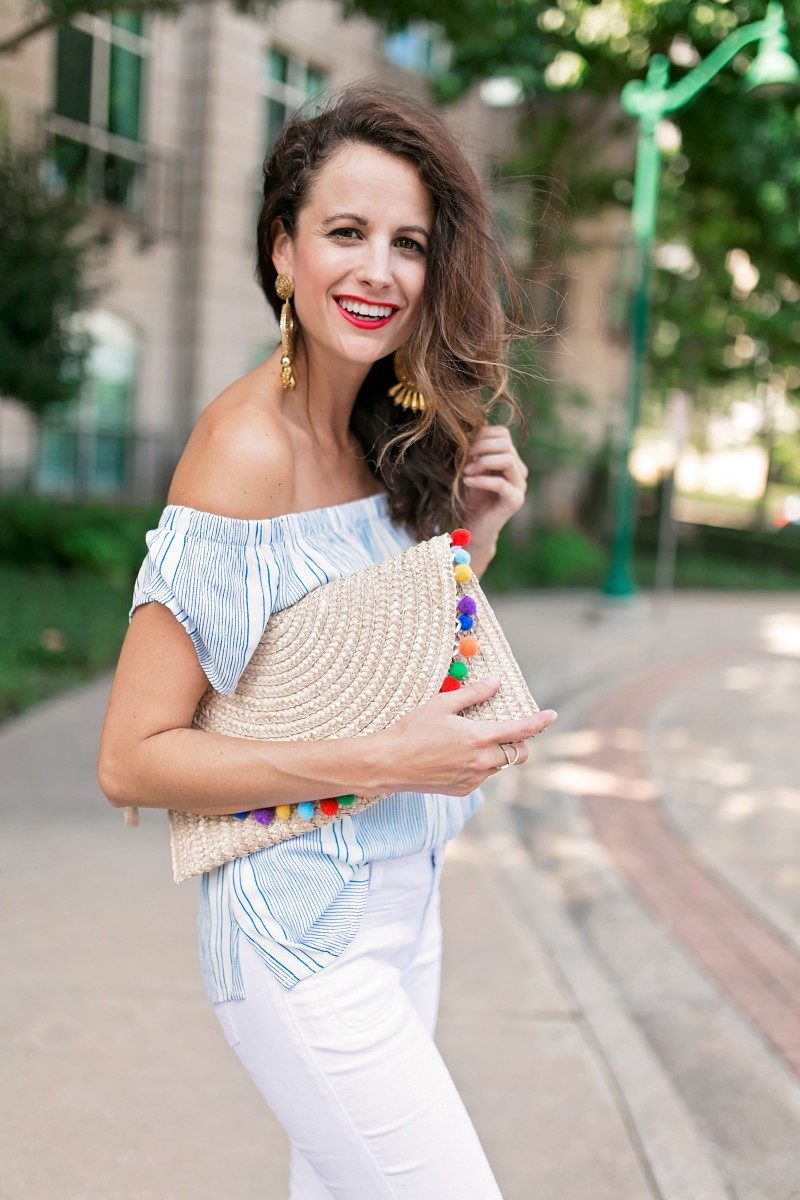 The Miller Affect wearing large gold tassel earrings and a holding a straw pom clutch
