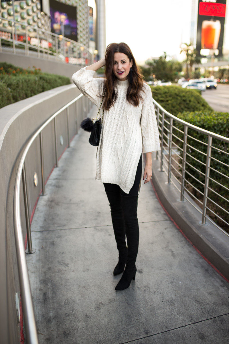 The Miller Affect wearing an ivory cable knit tunic and black over the knee suede boots