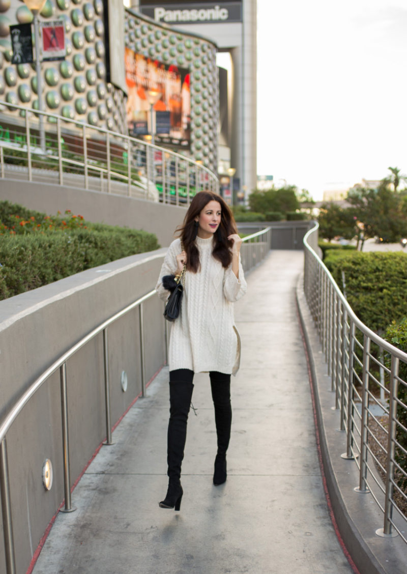 The Miller Affect wearing an ivory cable knit tunic and black over the knee suede boots