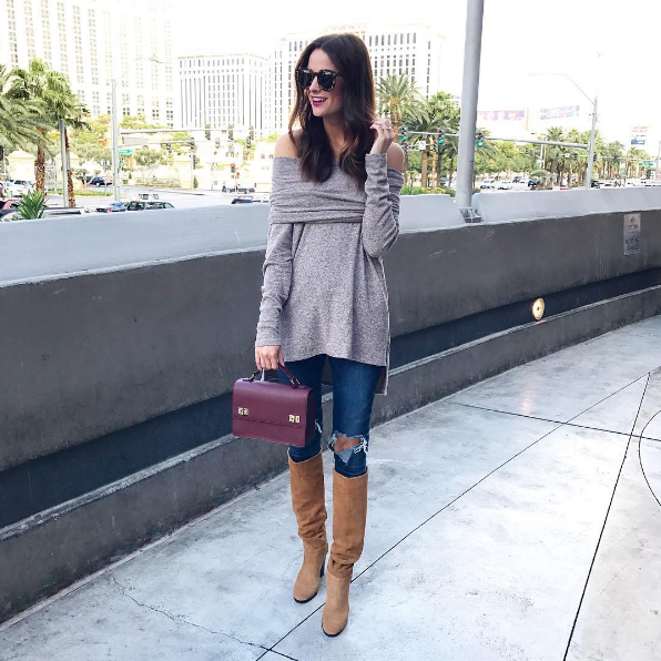 The Miller Affect wearing a tan soft sweater that can be worn on or off the shoulder and tan slouchy boots with a heel