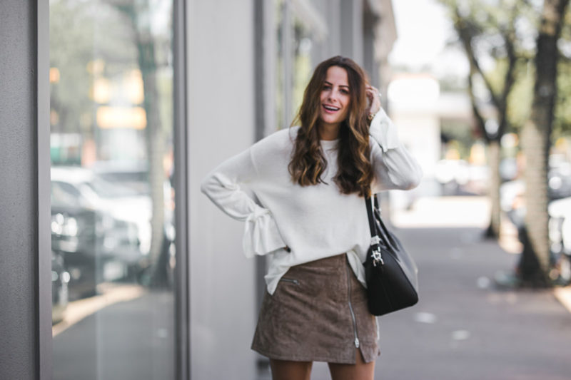 The Miller Affect wearing a white bell sleeve sweater and a suede mini skirt