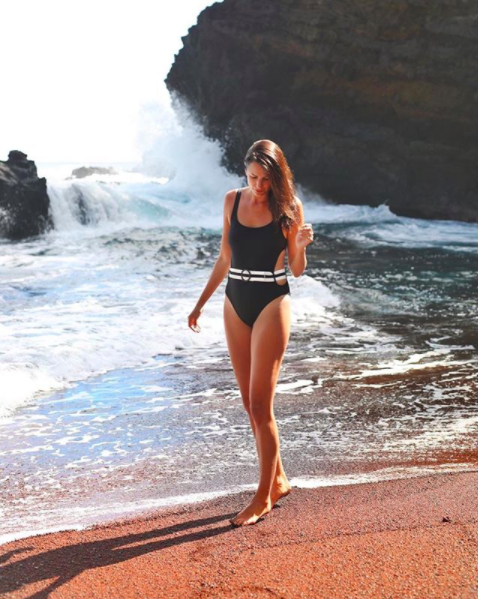 the miller affect wearing a black solid and striped one piece swimsuit