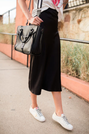 the miller affect wearing golden goose sneakers and a black midi skirt