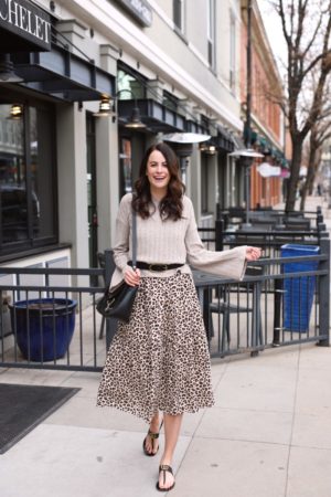 the miller affect wearing a beige knit sweater over a leopard maxi dress